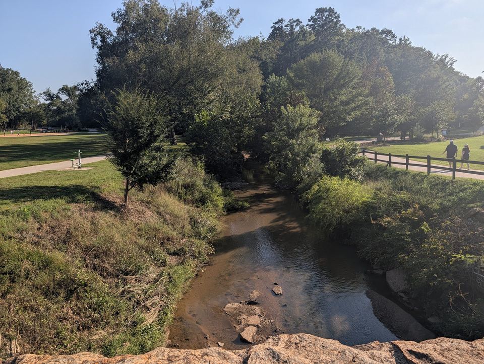 A shallow, rocky creek running between grassy, tree-lined banks.